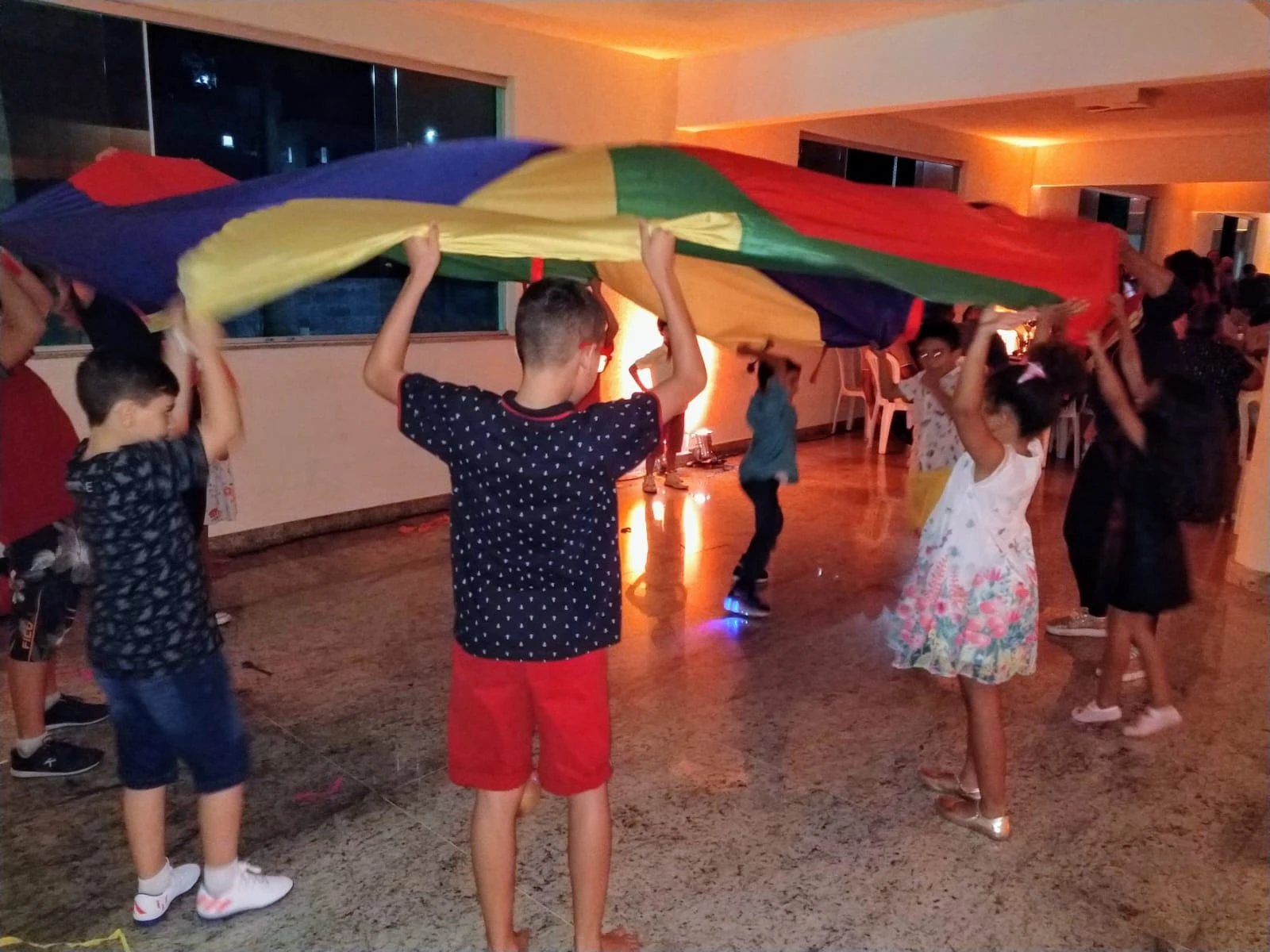 Crianças brincando de paraquedas colorido no Espaço Kids de uma festa de 15 anos