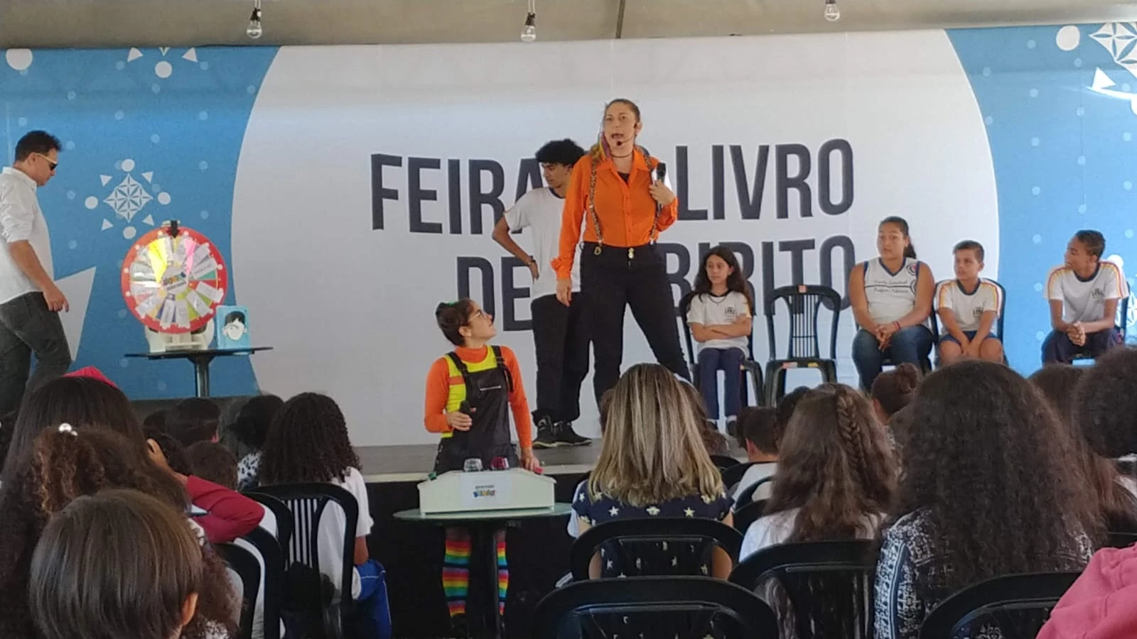 Recreadoras apresentando atividade no palco da Feira do Livro para uma plateia de estudantes